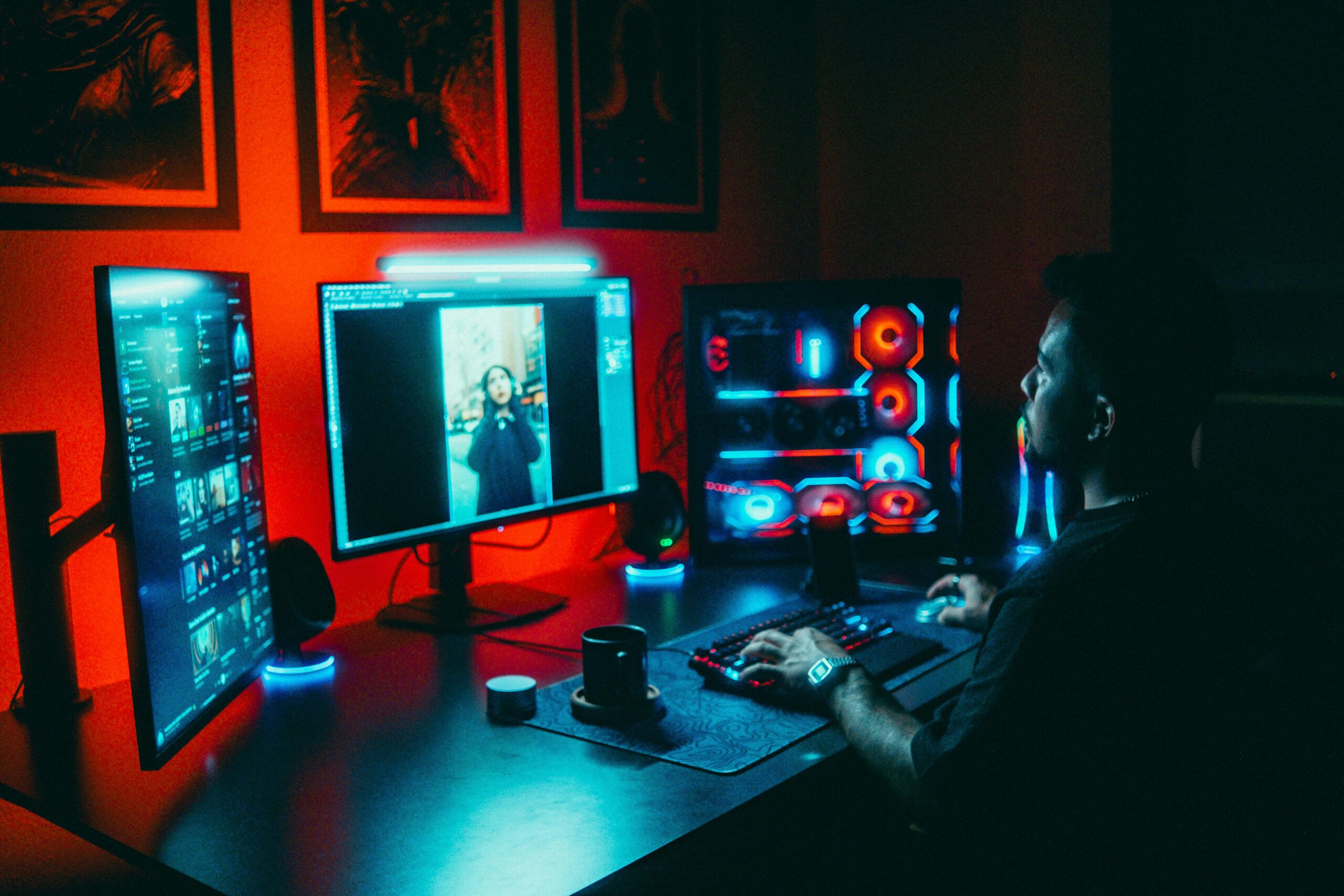 A young man working on a multi-screen computer setup in a dark, neon-lit room.